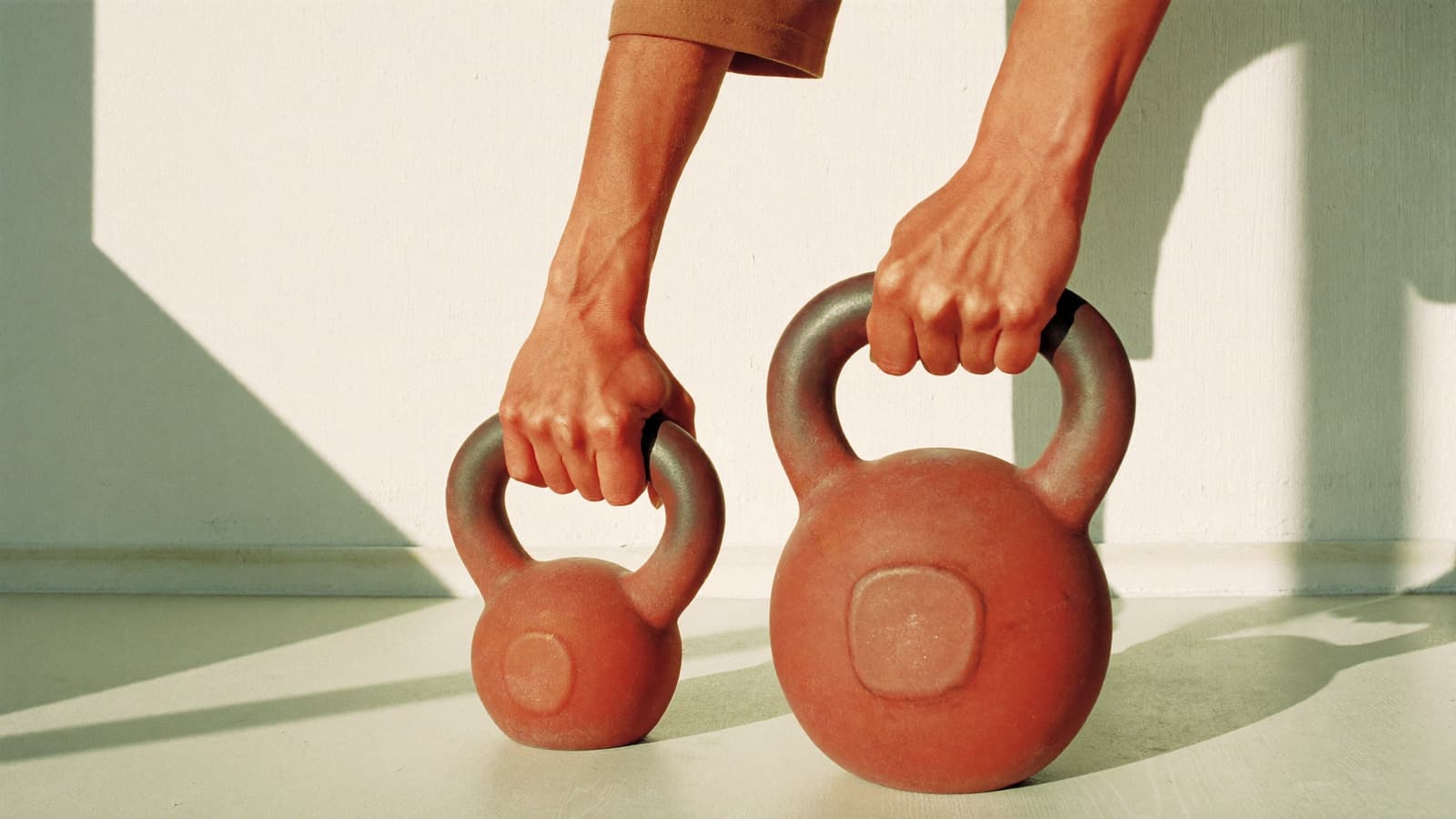 Chalked hands gripping two plain cast-iron kettlebells in warm morning light